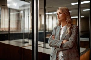 Zdjęcie jest ilustracją do artykułu: Prezes w Polsce to mężczyzna. Truizm? Niestety. Przedstawia bizneswoman opartą o ścianę z szyb w open space.