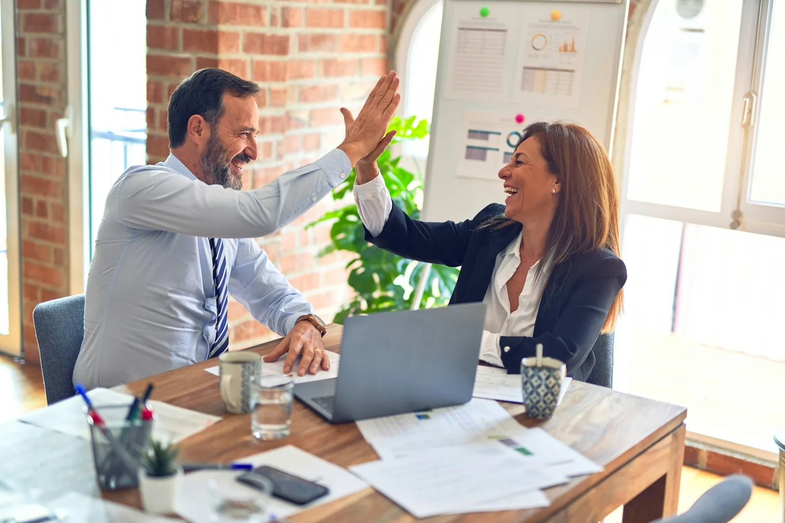 Two colleagues high-fiving across a desk after a successful hire