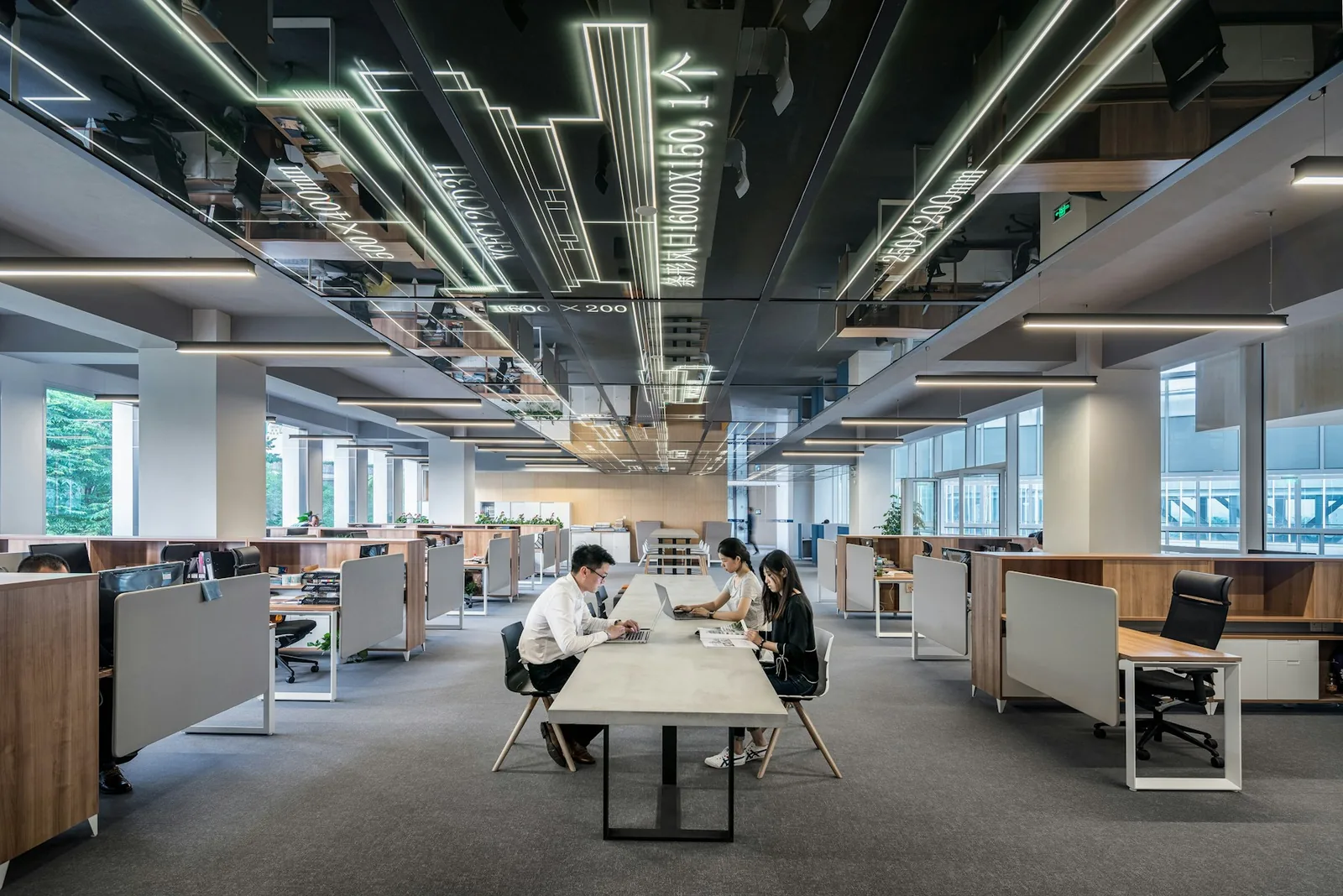 Open-plan office with a long shared table under a light-strip ceiling